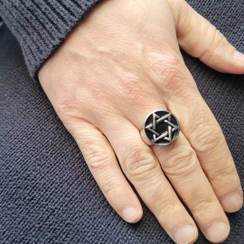 Primo piano dell'anello stella di David trasportato da un uomo che evidenzia il gioco leggero su acciaio lucido e lo sfondo nero