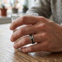 Vue de la bague portée à la main d'un homme, mettant en valeur les reflets de l'acier et le contraste profond du câble noir