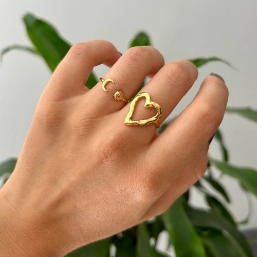 Bague romantique cœur ajouré doré portée au doigt, apportant une touche d'éclat à une tenue féminine.