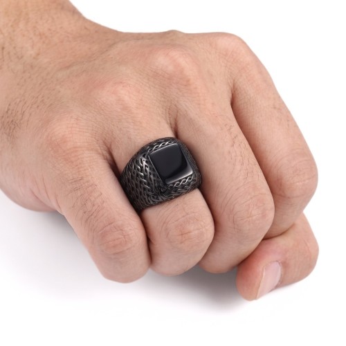 Anello a maglia nera strutturato portato a dita da un uomo, affermando uno stile moderno e misterioso.