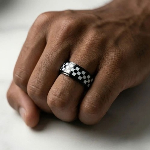Bague anti-stress en acier inoxydable à motif damier noir et blanc portée sur le poing d'un homme au style moderne.