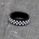 Détail de la bague homme anti-stress en acier noir avec anneau rotatif drapeau à damier posée sur une surface texturée.