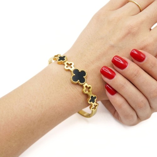Femme portant un bracelet jonc rigide en acier inoxydable doré, orné d'un trèfle central noir et de petits trèfles ajourés.