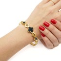 Frau, die ein starres Biss-Goldenes Edelstahl-Armband trägt, das mit einem schwarzen zentralen Klee und kleinen offenen Klee ges