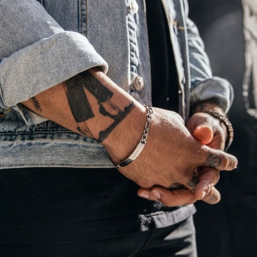 Man with arms crossed bearing the steel bracelet with mesh Figaro, highlighting the custom plate