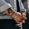 Homme avec les bras croisés portant le bracelet en acier à maille Figaro, mettant en évidence la plaque personnalisée