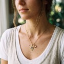 Donna che indossa collana d'acciaio dorata con pendente a mano di FATMA (BAD BLUE) e fascino rotondo trasparente.