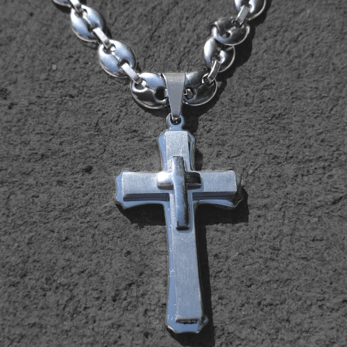 Pendentif homme trois croix superposées et chaine grains de café acier de près sur un mur